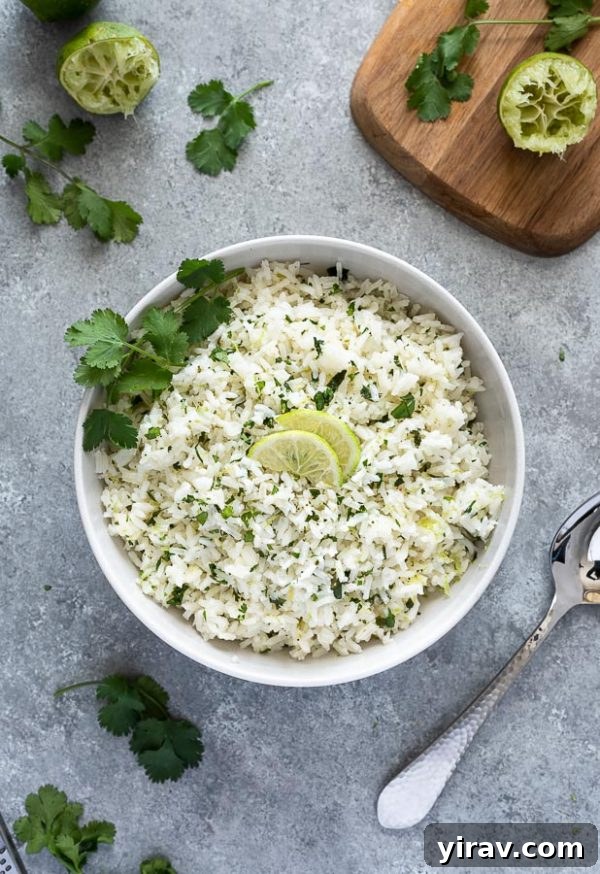 An overhead view of a bowl of homemade cilantro lime rice, artfully arranged with lime wedges and fresh cilantro leaves on top, emphasizing its vibrant freshness.