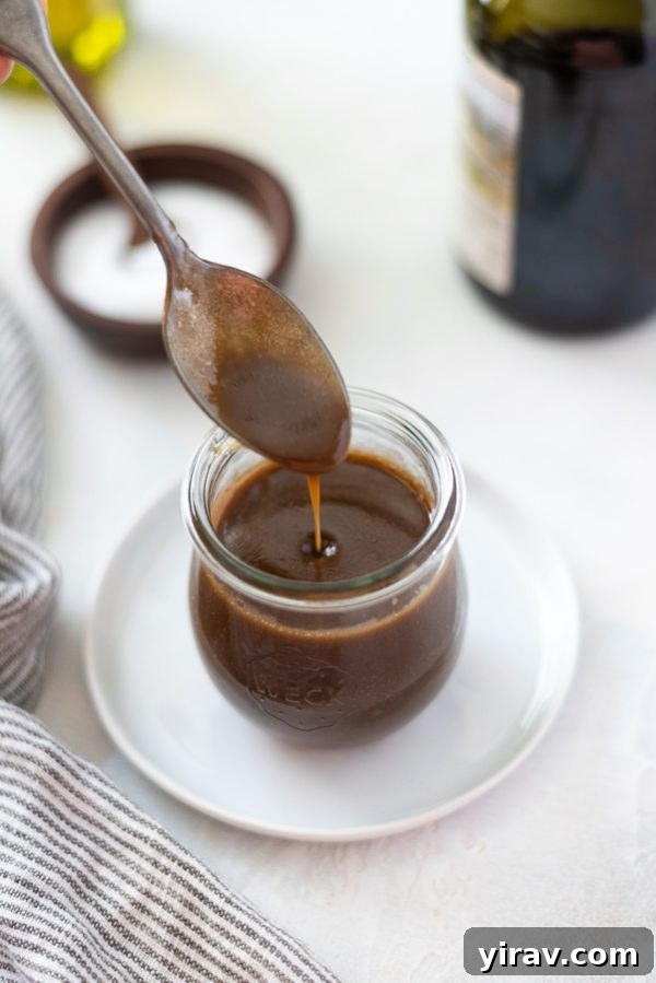Close-up overhead view of golden balsamic vinaigrette dressing being poured into a mason jar with a spoon.