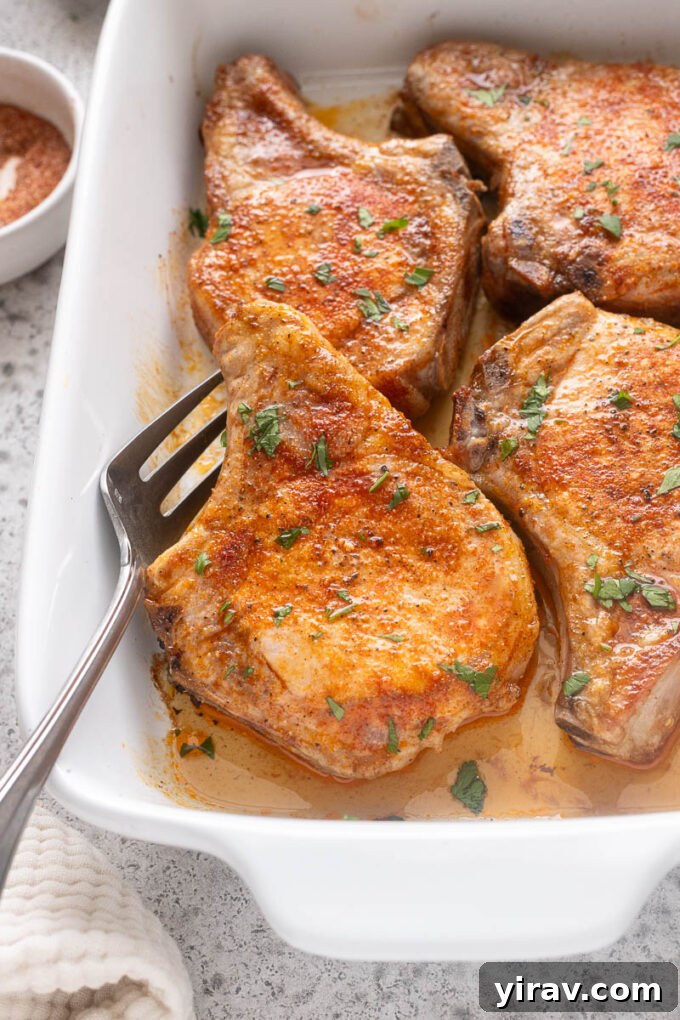 Tender Oven Baked Pork Chops 2 Oven baked pork chops in baking dish with serving fork.