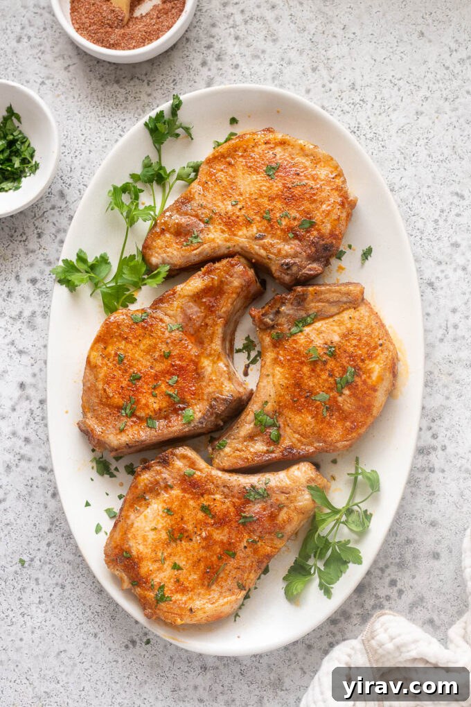 Tender Oven Baked Pork Chops 3 Baked bone-in pork chops on a serving platter with parsley.