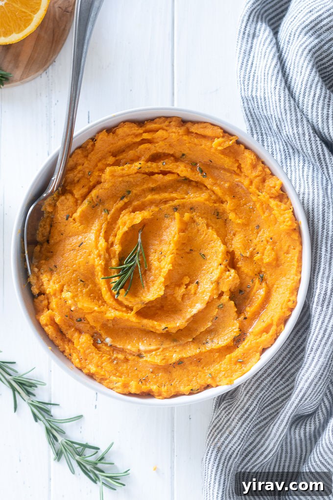 Close-up of creamy mashed sweet potatoes in a bowl, garnished with a fresh sprig of rosemary.
