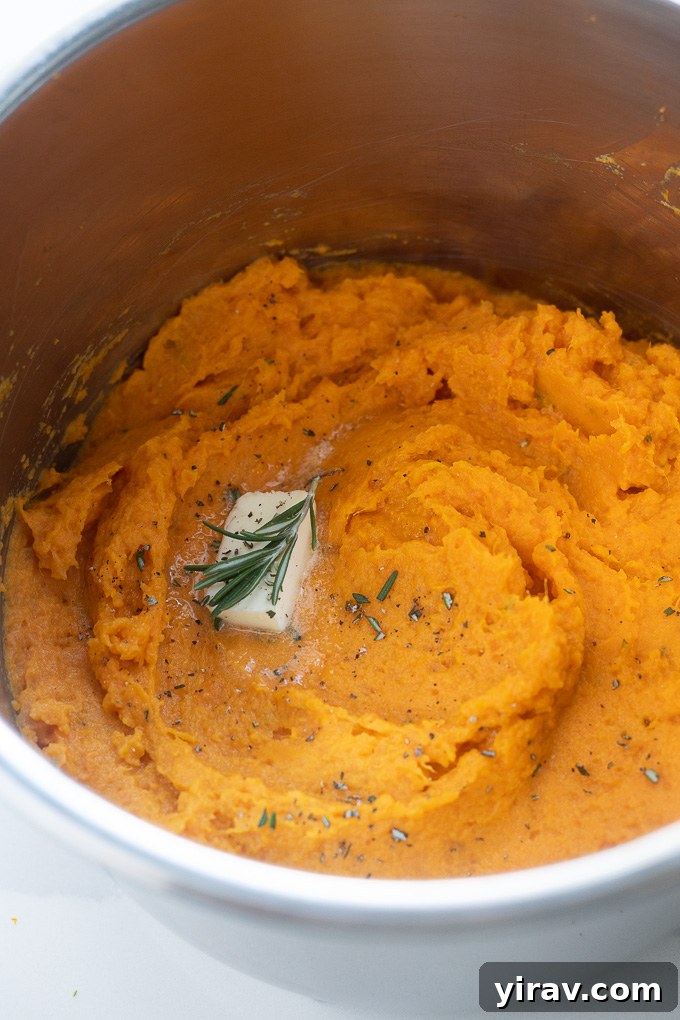 Close-up of creamy mashed sweet potatoes in an Instant Pot, topped with a pat of butter and fresh rosemary.