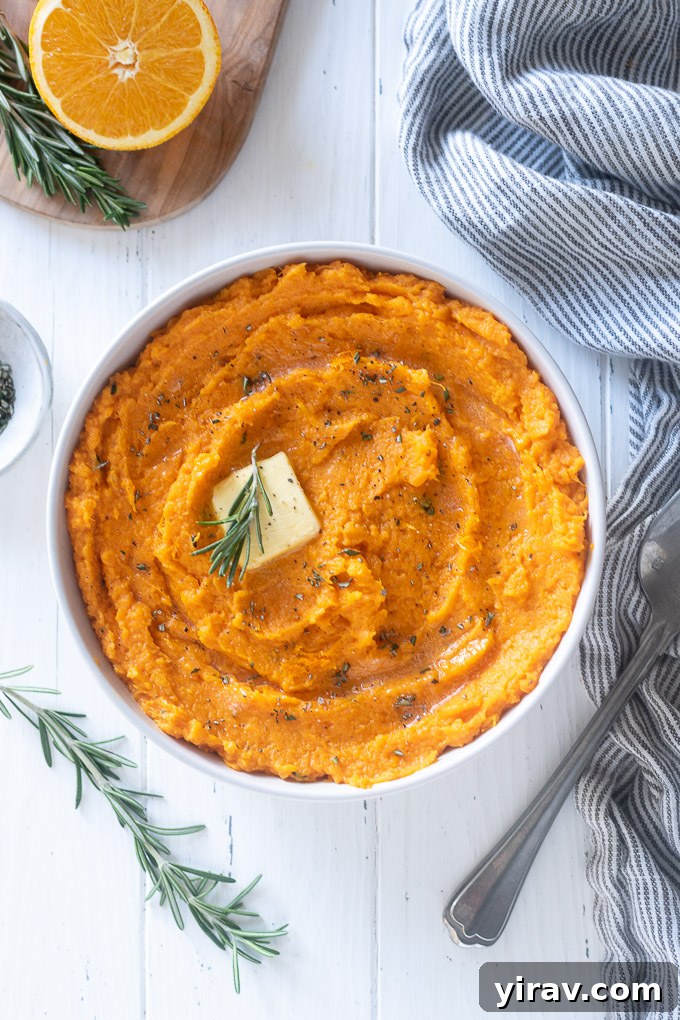 A serving of creamy mashed sweet potatoes topped with a melting pat of butter and fresh rosemary sprigs.