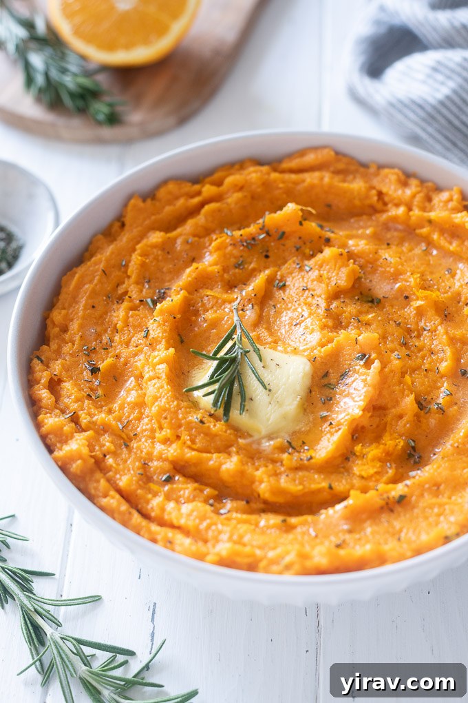 A bowl of creamy mashed sweet potatoes, garnished with a pat of melting butter and fresh rosemary.