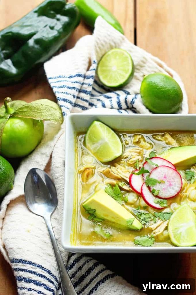 Overhead view of a vibrant bowl of traditional Mexican Chicken Pozole garnished with fresh lime wedges.
