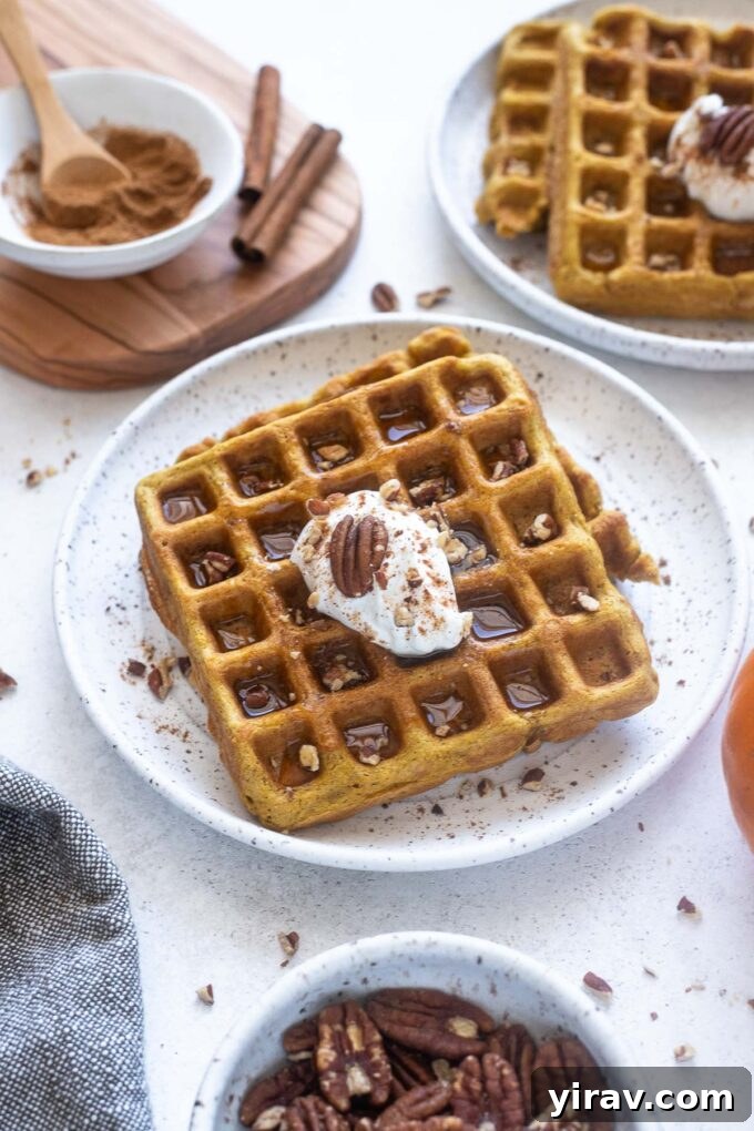 A close-up of a pumpkin spice waffle on a plate, topped with a dollop of yogurt and chopped pecans, ready to be eaten.