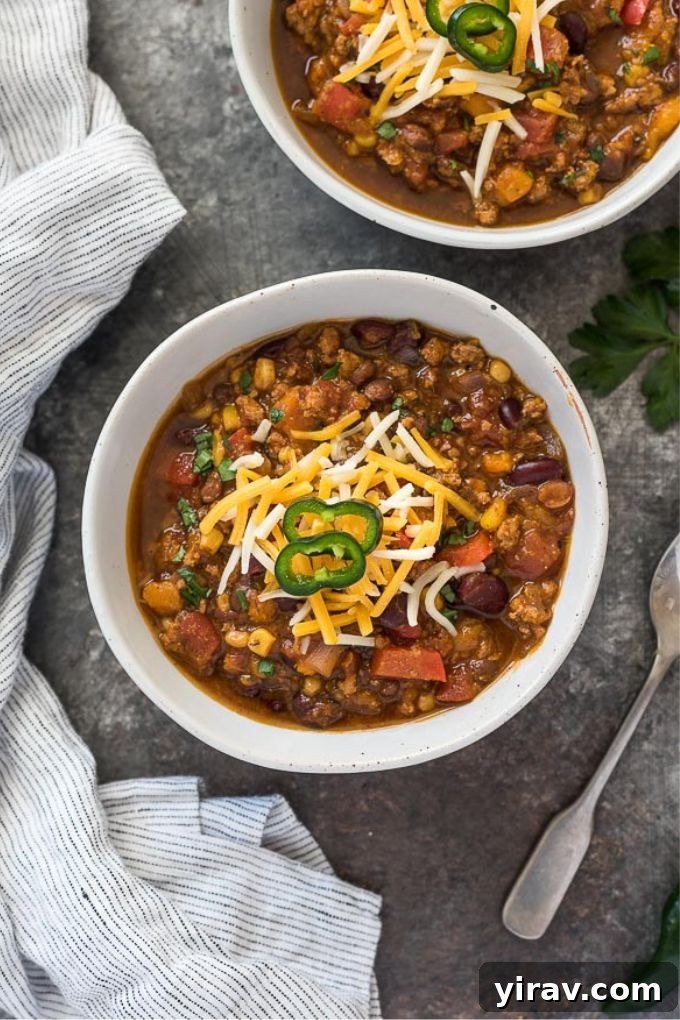Close-up of a bowl of pumpkin chili generously topped with shredded cheese and sliced jalapeños, showcasing its rich texture and vibrant colors.