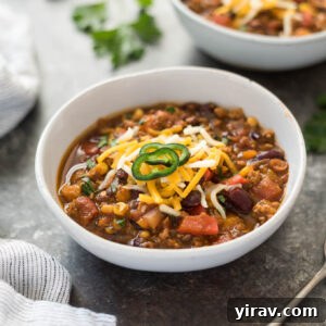 A top-down view of a rustic bowl filled with rich pumpkin chili, garnished with a dollop of sour cream and a sprig of cilantro, ready to be served.