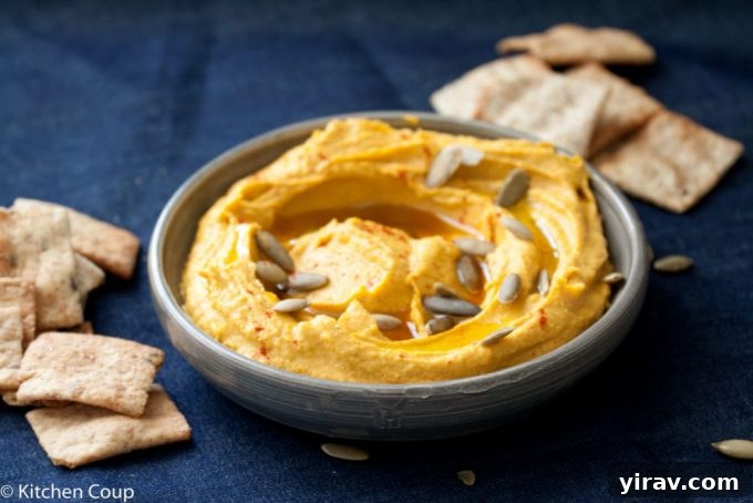 A dish of kabocha squash hummus surrounded by pita chips, on a dark blue background.