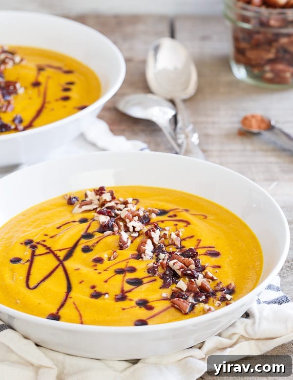 Two bowls of creamy kabocha squash soup topped with pecans and a cherry drizzle.