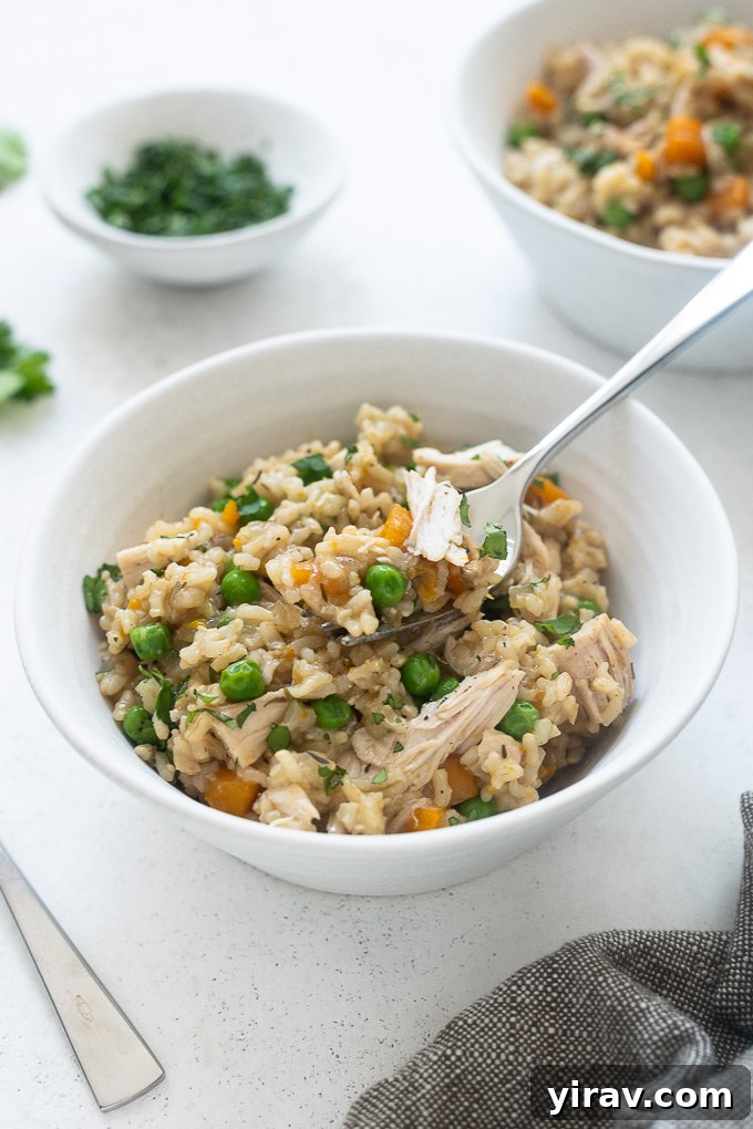A fork digging into a bowl of Instant Pot chicken and rice, showing the texture of the chicken and rice.