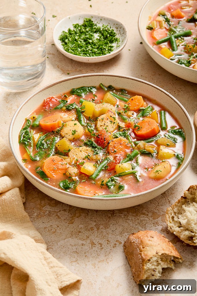 A bowl of fresh Instant Pot Vegetable Soup served with crusty bread and garnished with parsley.