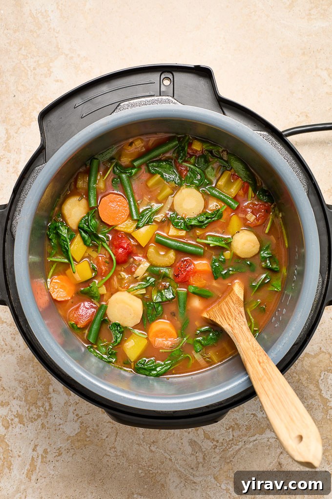 A wooden spoon stirring a rich, chunky vegetable soup inside an Instant Pot.
