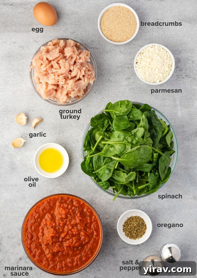 A collection of fresh ingredients laid out for baked turkey meatballs, including ground turkey, spinach, feta, and herbs.