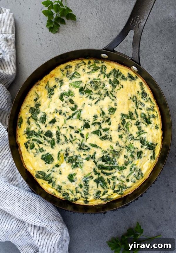 Overhead shot of a vibrant spinach and feta frittata, fresh from the oven, with a golden-brown top and slightly puffed appearance.