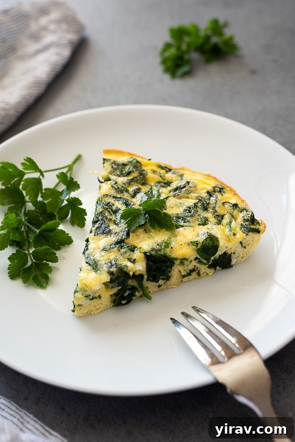 A perfectly portioned slice of spinach feta frittata on a white plate, garnished with fresh parsley.