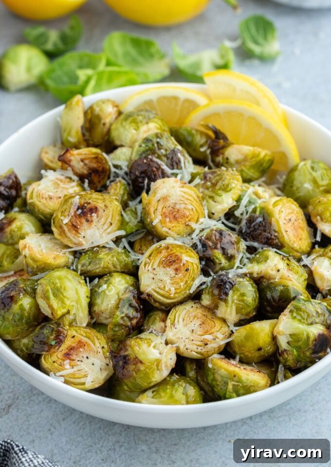 Crispy Air Fryer Brussels Sprouts 2 A bowl of golden-brown air fryer Brussels sprouts garnished with fresh lemon wedges and shredded Parmesan cheese, ready to serve.