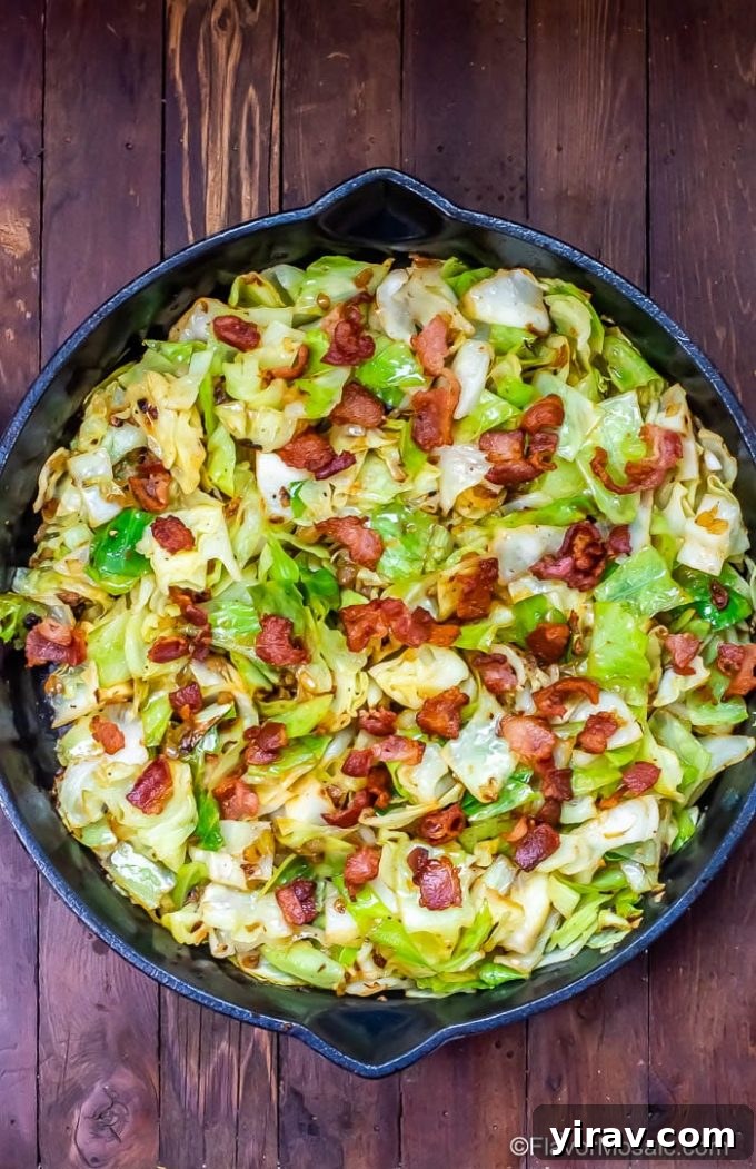 Overhead view of sizzling fried cabbage with crispy bacon in a cast iron skillet.