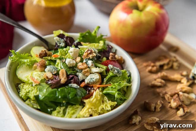 A refreshing Apple Cabbage Salad with walnuts and gorgonzola in a white bowl, with an apple in the background.