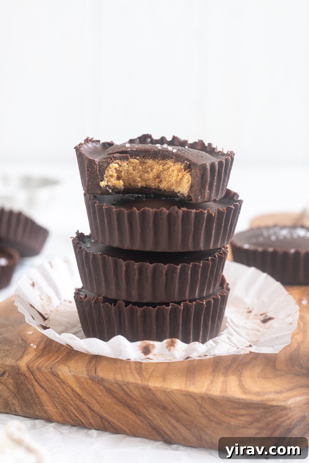 Stack of protein peanut butter cups on a cutting board with flaky sea salt scattered around.