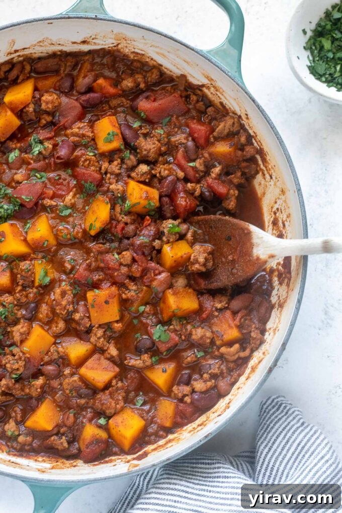 Hearty Butternut Turkey Chili 6 A wooden spoon stirring a pot of rich Butternut Squash Turkey Chili, showcasing its thick and chunky texture.