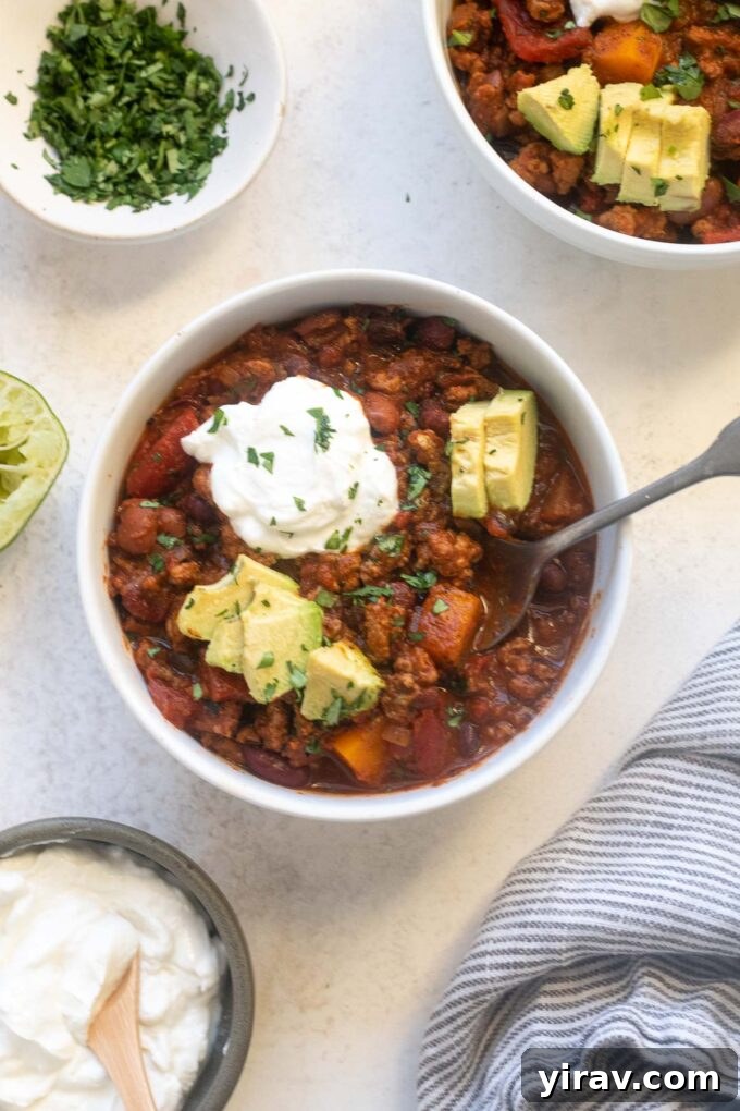Hearty Butternut Turkey Chili 7 A close-up of Butternut Squash Turkey Chili in a bowl, generously topped with creamy avocado slices and a dollop of sour cream.