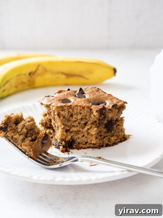 Golden Banana Bites 6 A square slice of banana oat cake on a small white plate with a fork.