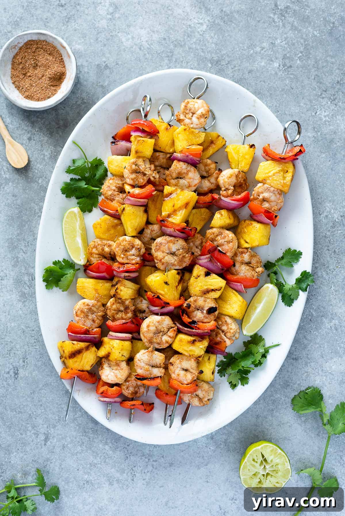 Overhead shot of vibrant Jerk Pineapple Shrimp Skewers arranged on a rustic serving platter, garnished with fresh cilantro and lime wedges.