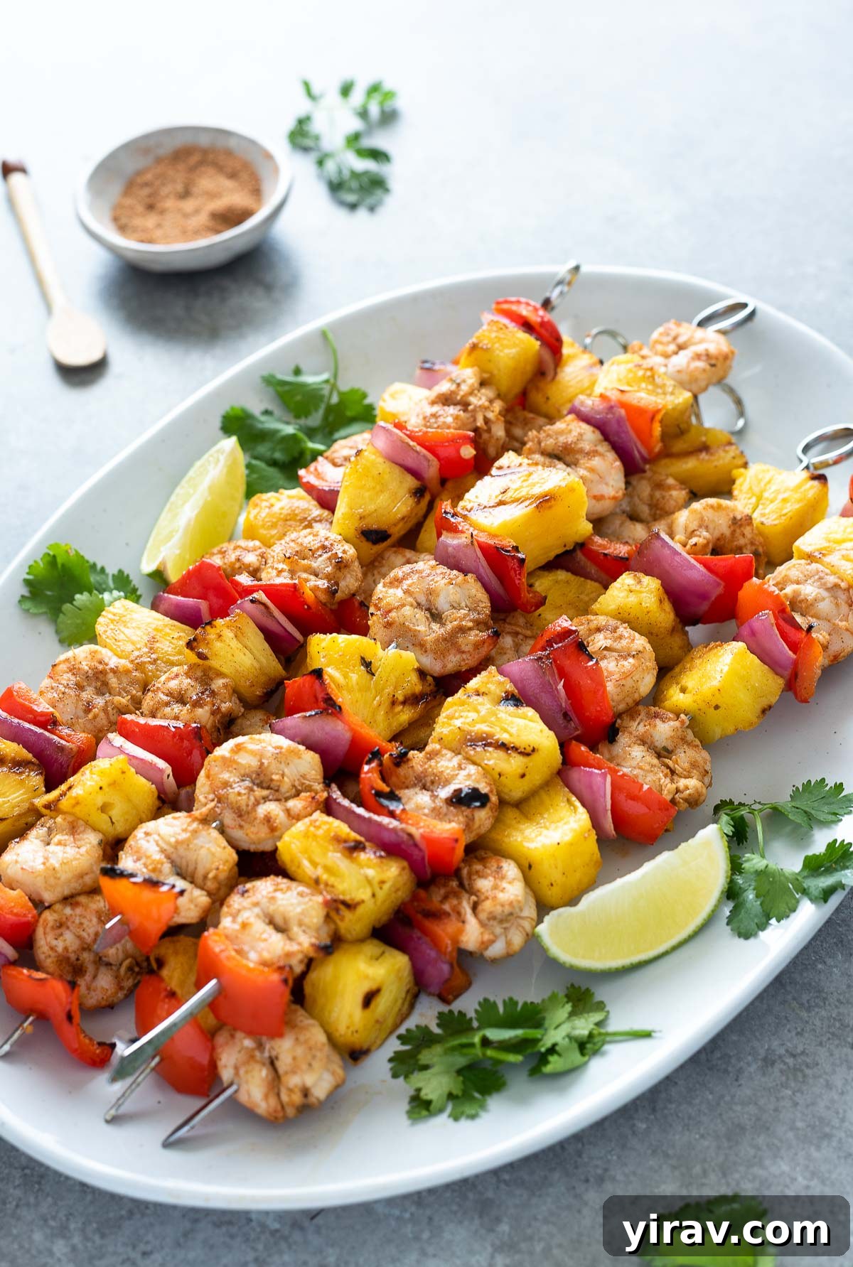 Close-up front view of perfectly grilled pineapple shrimp skewers artfully arranged on a platter, garnished with fresh cilantro and bright lime wedges.