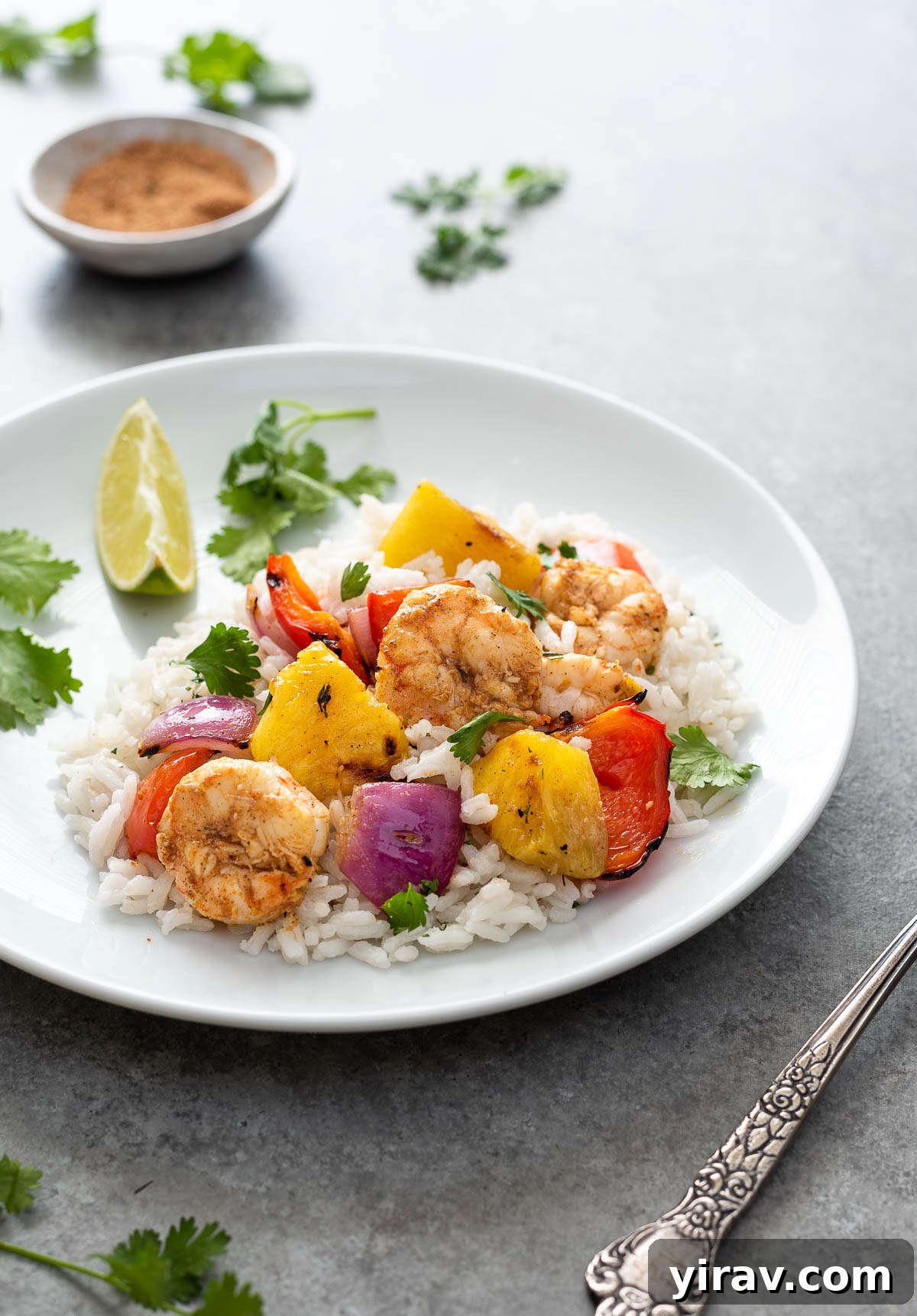A beautiful serving of grilled Jerk Pineapple Shrimp Skewers presented over a bed of fluffy white rice on a clean white plate, garnished with fresh herbs.