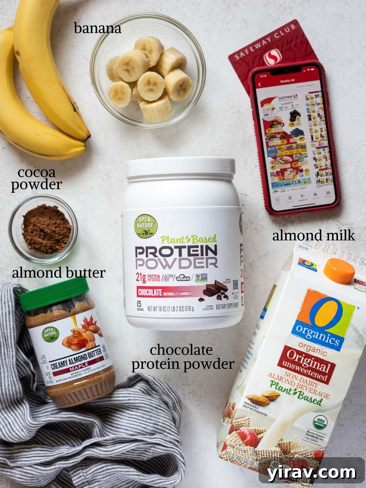 A flat lay photograph displaying the five simple ingredients needed for the chocolate banana protein smoothie: almond milk, frozen banana chunks, chocolate protein powder, almond butter, and cocoa powder.