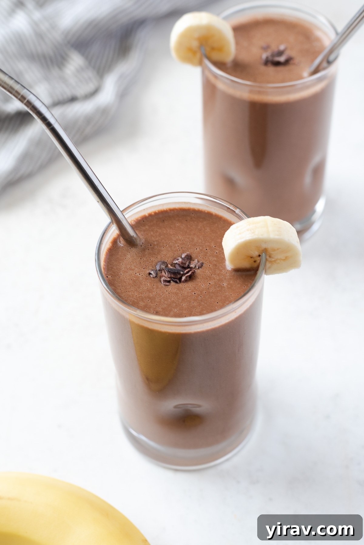 A stylish glass filled with a rich chocolate banana protein smoothie, topped with a sprinkle of cacao nibs and a banana slice, highlighting its appeal as a gourmet breakfast or snack.