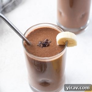 Close-up of a chocolate banana protein smoothie in a glass with a metal straw and a banana slice on the rim, illustrating its inviting texture.