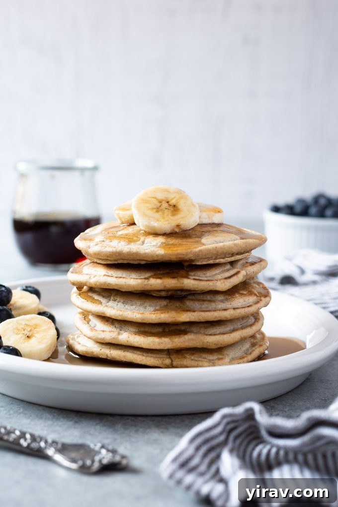 Stack of oat flour pancakes on a plate with fresh fruit and syrup