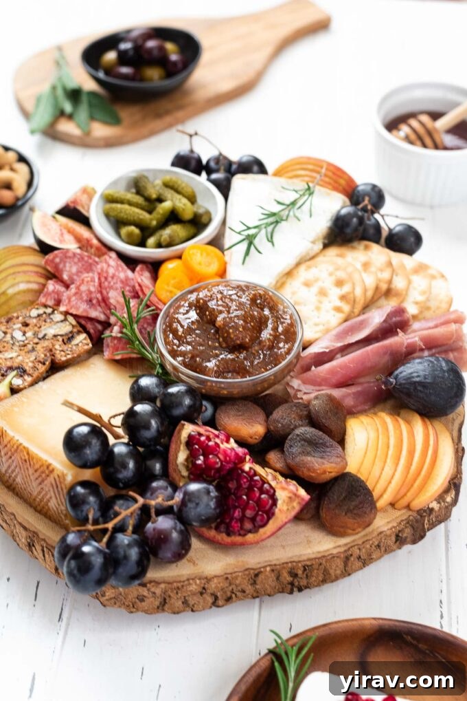 A vibrant fall-themed charcuterie board overflowing with artisan cheeses, cured meats, fresh grapes, figs, apples, nuts, and a variety of crackers, garnished with fresh rosemary.