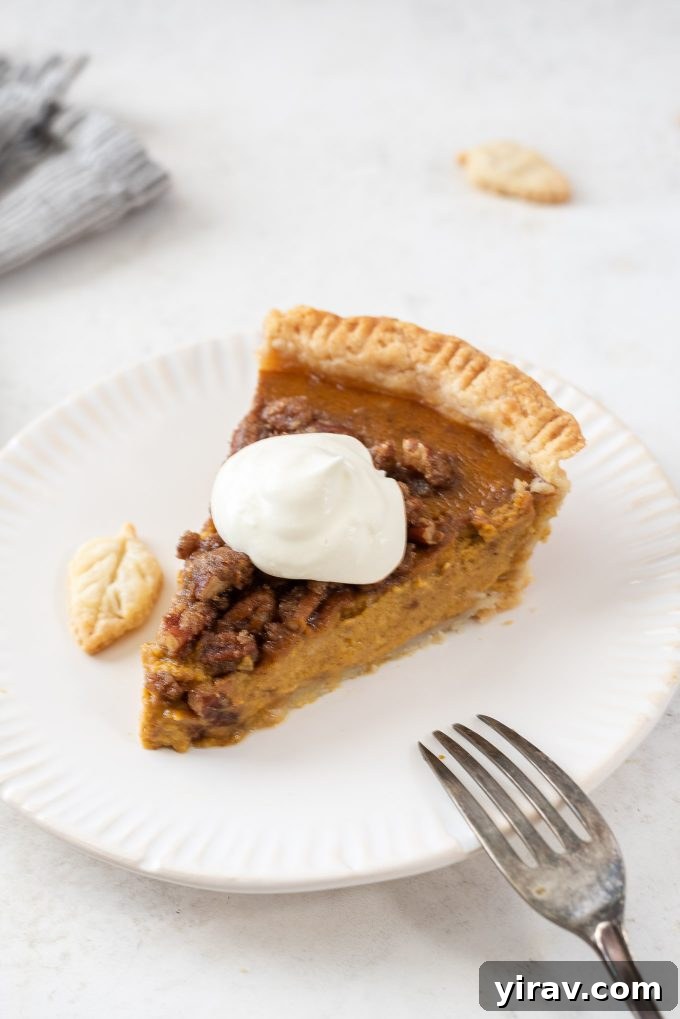 A slice of Pumpkin Pecan Pie, beautifully garnished with a swirl of whipped cream, on a white plate.