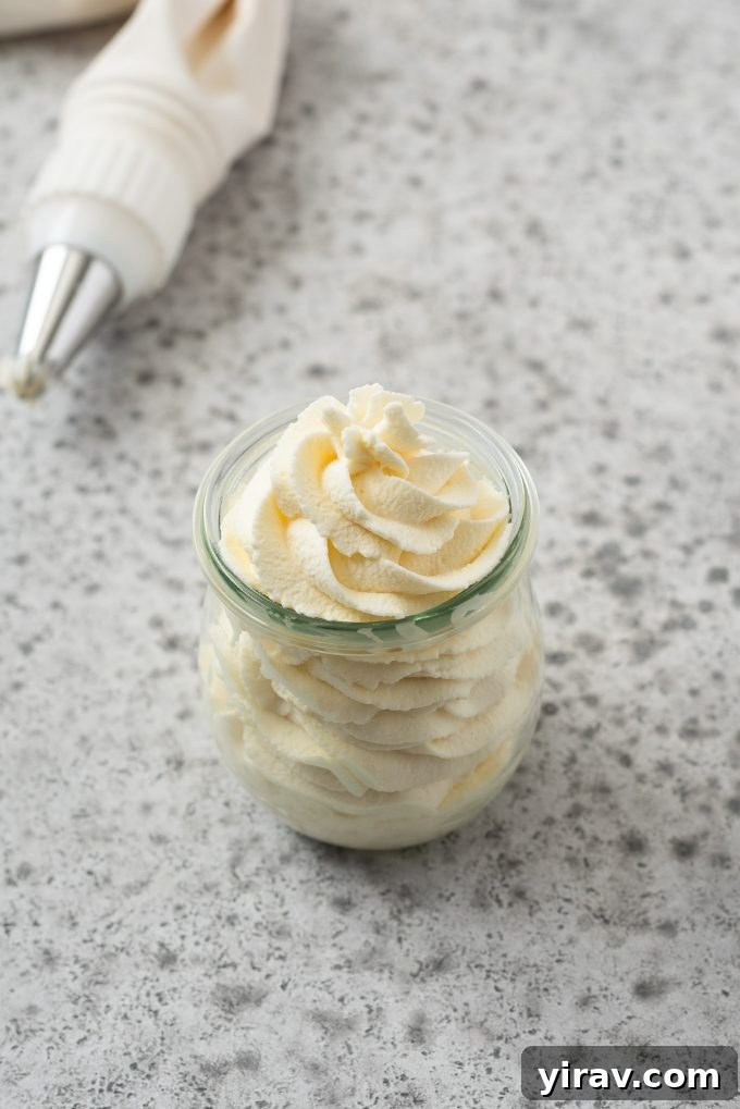 An angled view of a glass jar generously filled with expertly piped homemade whipped cream, showcasing its fluffy texture.