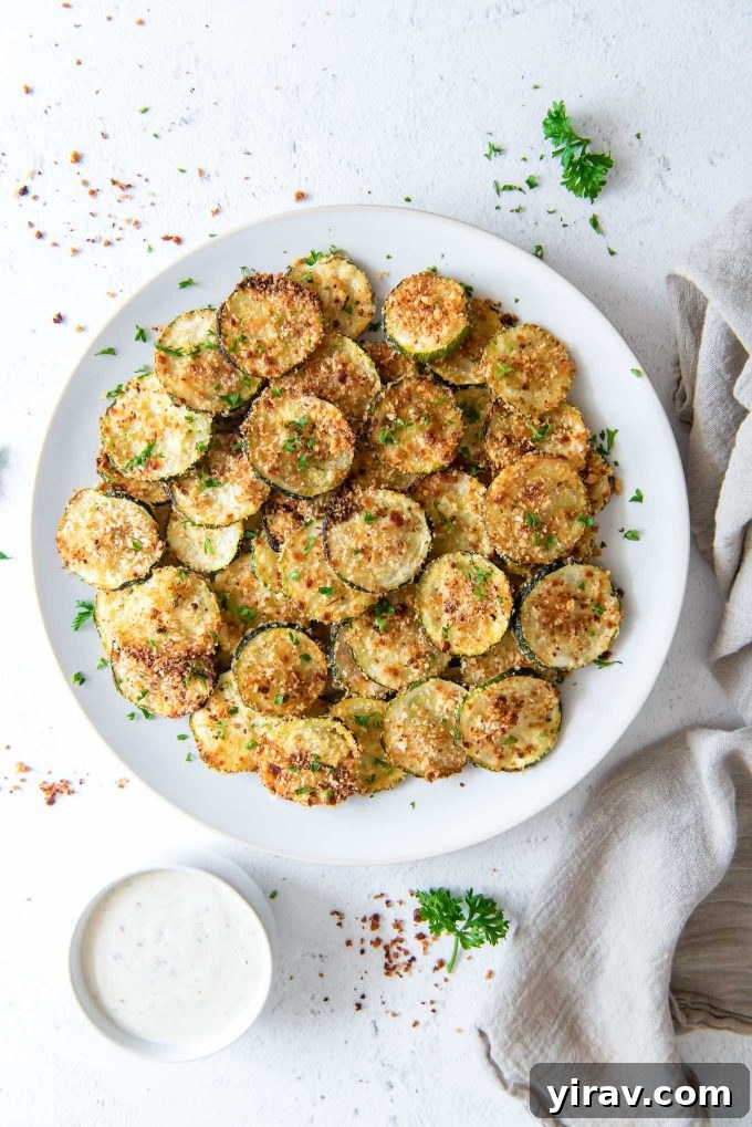 Oven Baked Zucchini Crisps 2 Perfectly golden oven-baked zucchini chips arranged on a white plate with a rustic linen napkin alongside.