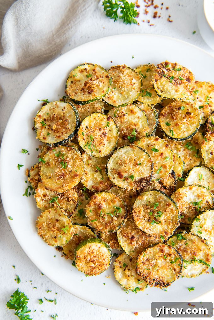 Oven Baked Zucchini Crisps 3 A close-up view of perfectly baked zucchini chips, golden and crispy, served on a round white plate.