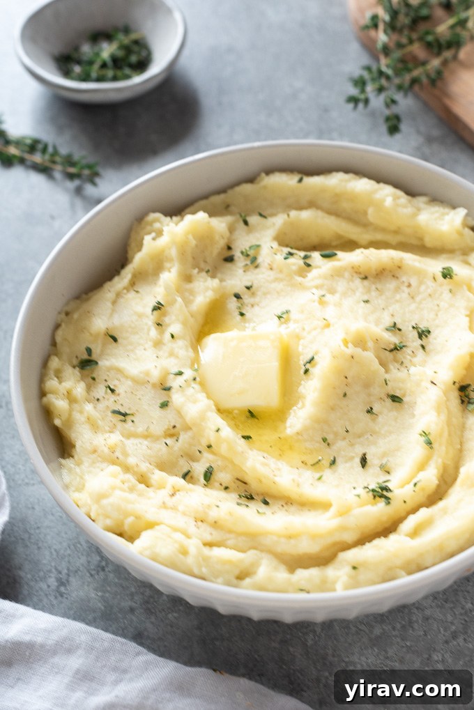A close-up of parsnip puree in a white serving bowl, garnished with a pat of butter melting and fresh thyme leaves.