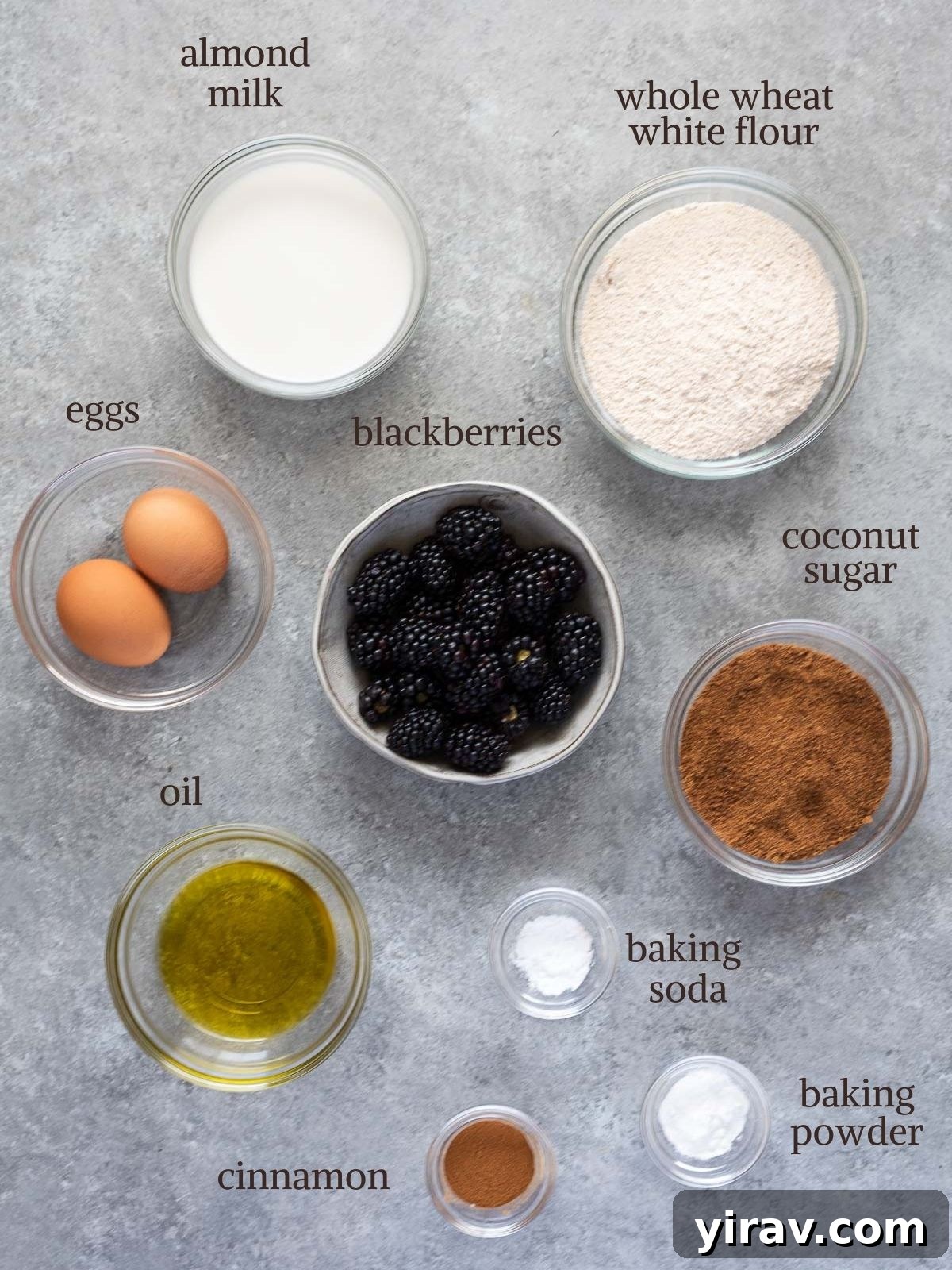 A selection of fresh ingredients laid out on a table, including blackberries, whole wheat flour, coconut sugar, eggs, and milk, ready for baking healthy muffins.