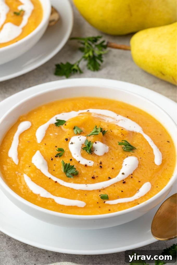 Close-up of a bowl of roasted butternut squash and pear soup garnished with a swirl of coconut milk and fresh herbs