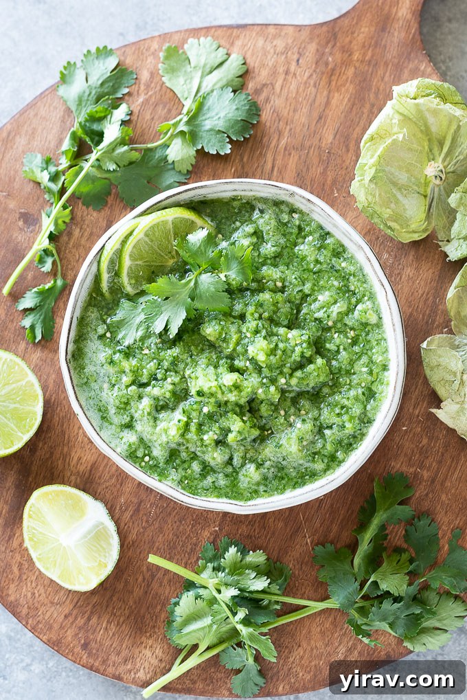 A pristine white bowl filled with vibrant green salsa, adorned with lime wedges and fresh cilantro leaves
