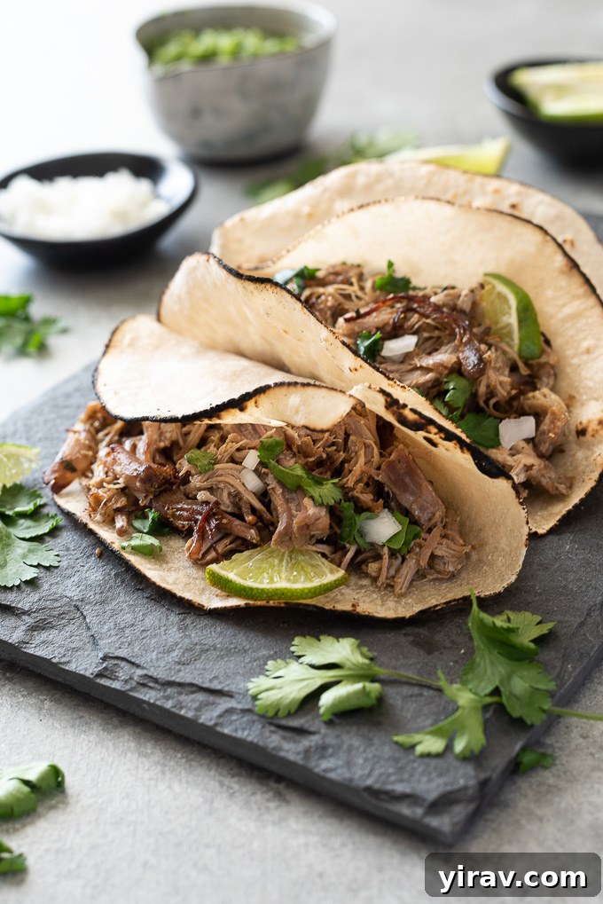 Slow cooker pork carnitas tacos on plate with diced onion, cilantro and lime
