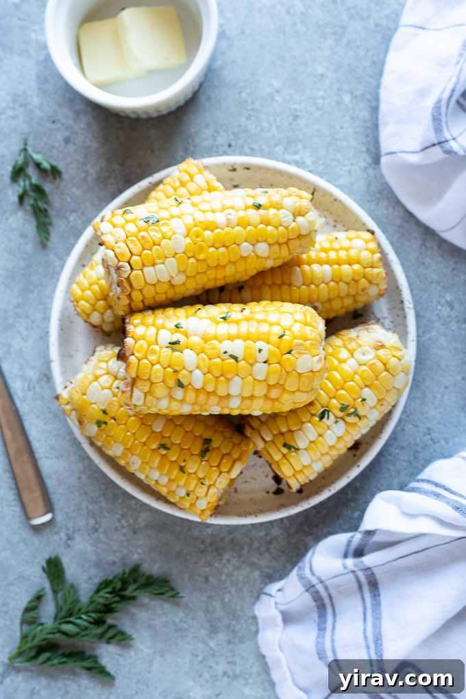 Golden Air Fryer Corn 3 Air fryer corn on the cob on a white plate with butter and parsley