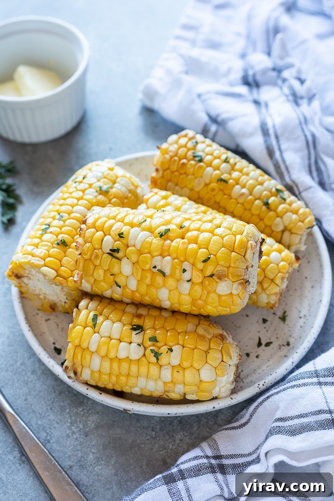 Golden Air Fryer Corn 7 Air fryer corn on the cob on a serving plate with a linen alongside