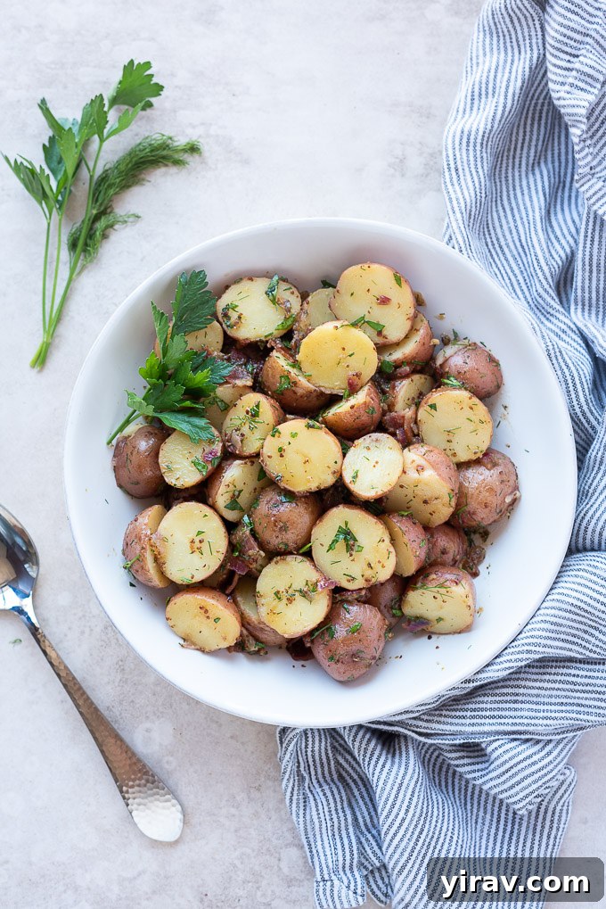 A close-up of German potato salad in a rustic white bowl, garnished with fresh dill and parsley, sitting on a linen cloth.