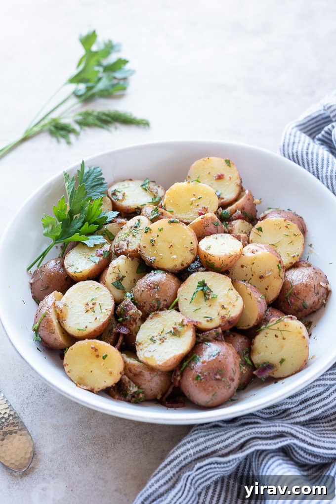 Warm German potato salad served in a elegant white bowl, garnished generously with fresh parsley and dill, ready for a meal.