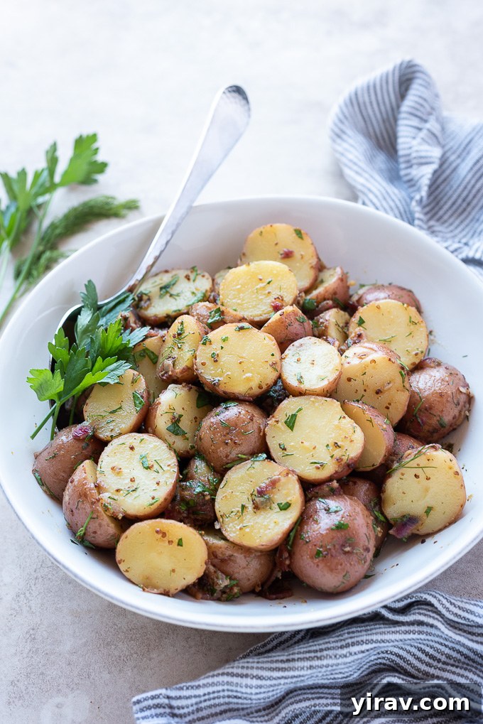 A warm German potato salad in a white serving bowl, with a wooden serving spoon, garnished with fresh herbs.