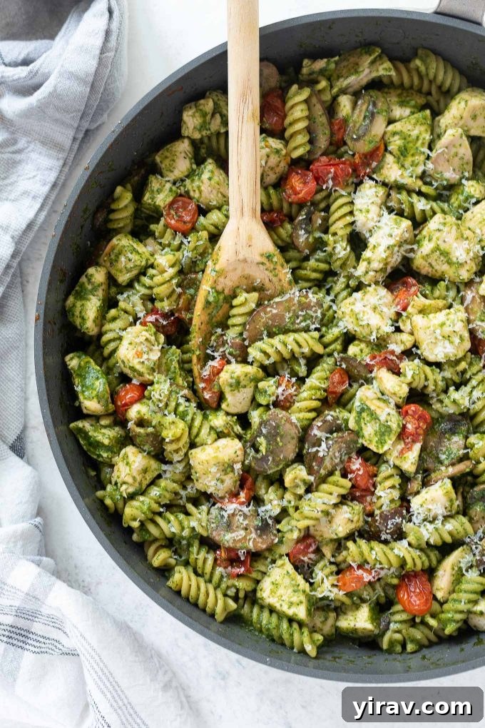 Chicken pesto pasta in a skillet with wooden spoon, showcasing a hearty, easy meal.